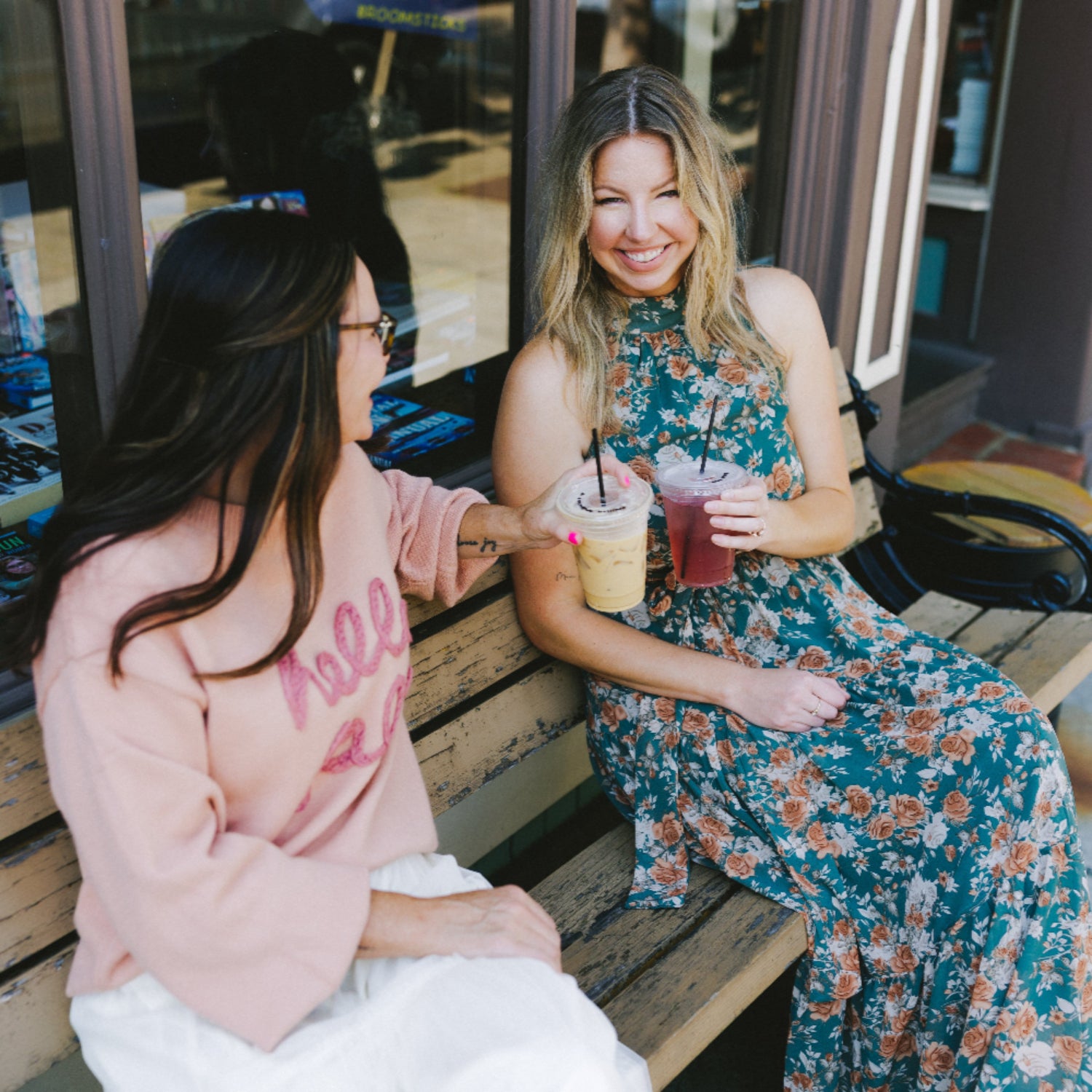 Women in fall outfits- hello fall sweater with skirt and floral maxi dress- sitting on bench with drinks