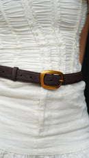 Close-up of a white textured dress with an elegant brown suede waist belt with curved gold buckle