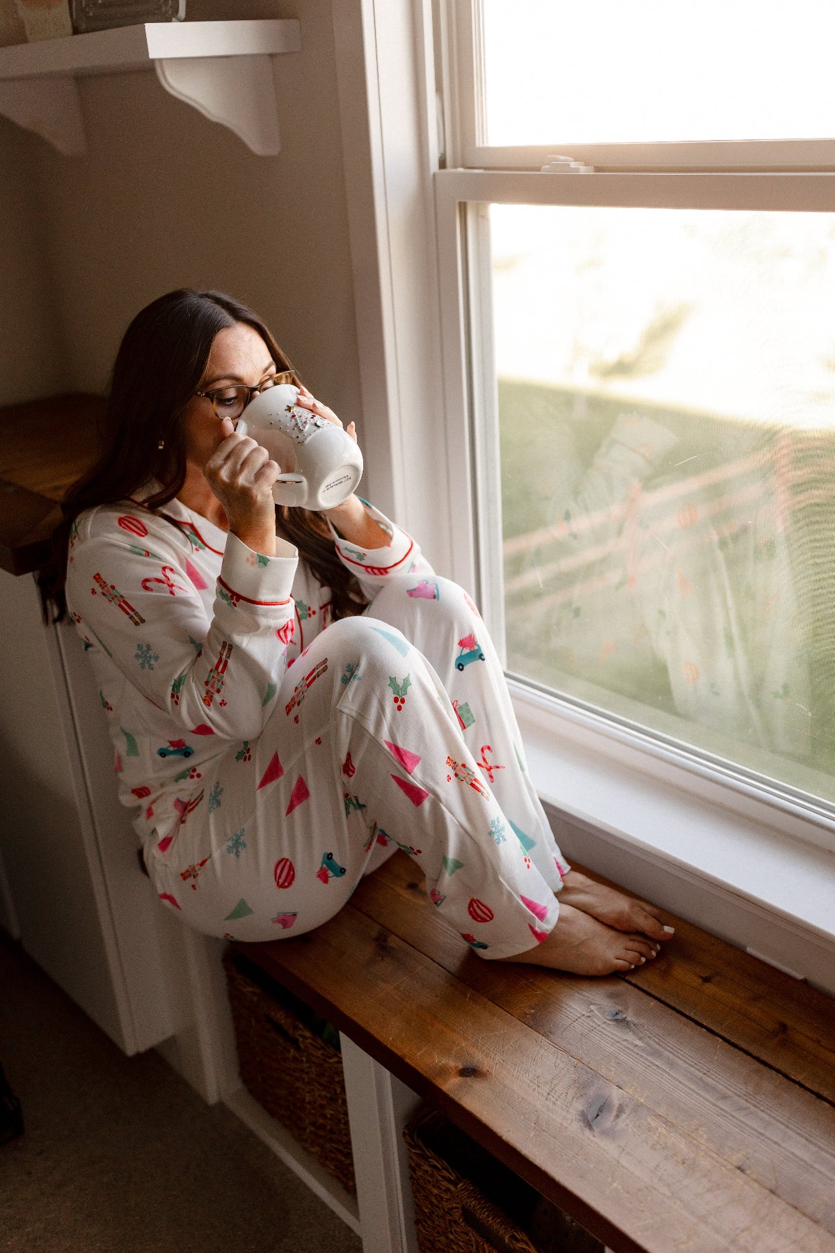 Woman in CHRISTMAS LONG SLEEVE 2 PC PAJAMA SET sitting by a window drinking from a mug