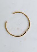 gold open bangle bracelet with sleek minimalist design on neutral background