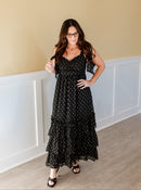 Woman wearing a black polka dot dress standing against a beige wall.