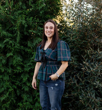 Woman wearing a plaid shirt and jeans standing in front of green bushes