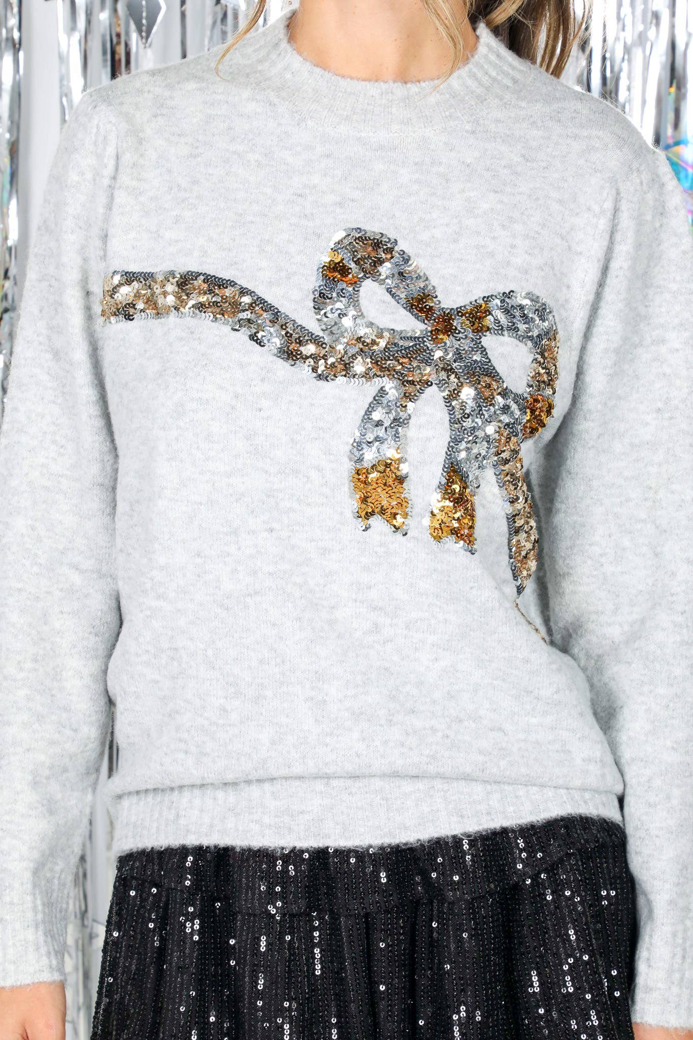 Gray sweater with a decorative bow design featuring sequins, worn by a woman.