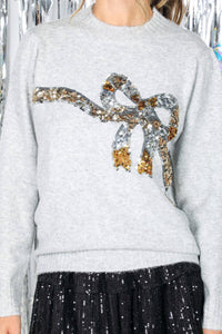 Gray sweater with a decorative bow design featuring sequins, worn by a woman.