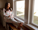 Woman in Christmas pajamas sitting by a window, looking out.