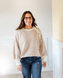 Woman wearing a geometric patterned sweater and jeans in a room with white walls and a light-colored floor.