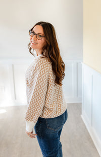 Woman wearing a geometric patterned sweater and jeans standing in a room with white walls and a yellow wall.