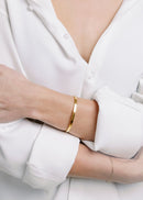 model wearing thin gold cuff bracelet featuring a polished open-ended style