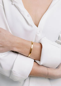 model wearing thin gold cuff bracelet featuring a polished open-ended style