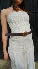 Woman wearing a strapless white dress with a classic chocolate brown suede belt against a dark background