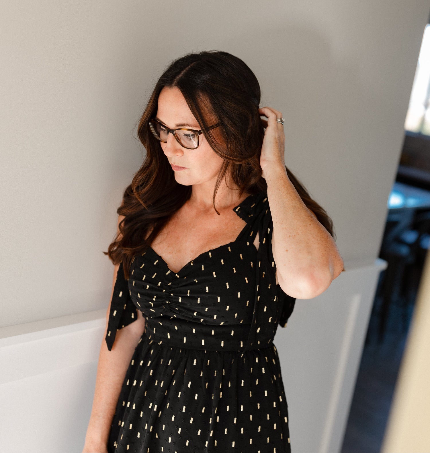 Woman adjusting her hair in a black dress with gold dots.